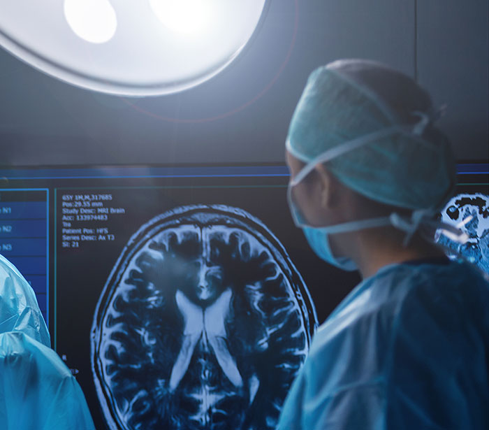 Surgeon in scrubs and mask analyzing brain MRI scans under surgical light in a medical operating room setting. Surgeon in scrubs and mask analyzing brain MRI scans under surgical light in a medical operating room setting.