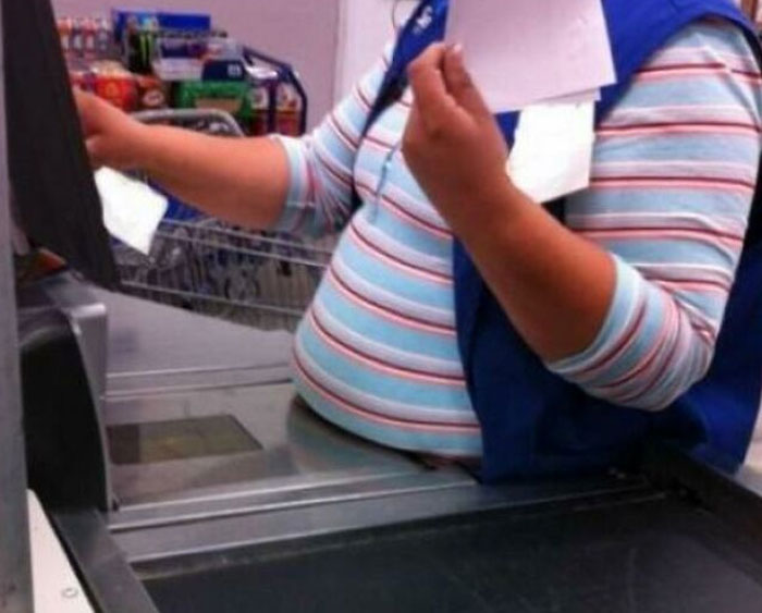 Walmart employee with striped shirt and blue vest scanning items at checkout in a busy store environment