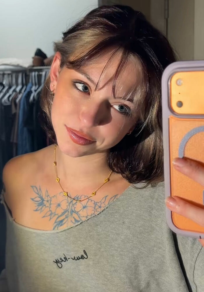 Young woman taking a mirror selfie after removing her nose ring, trending online for political appearance comments. Young woman taking a mirror selfie after removing her nose ring, trending online for political appearance comments.