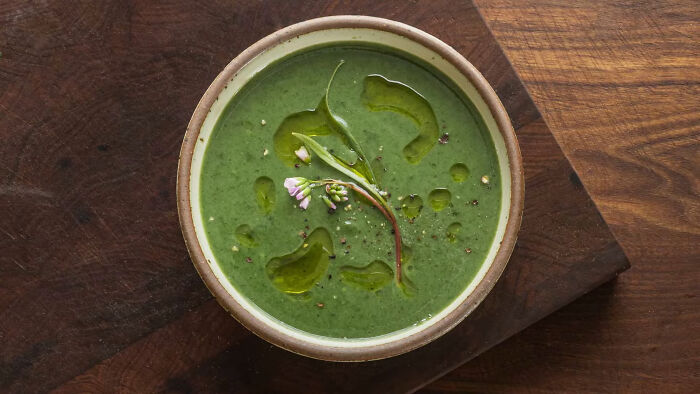 Bowl of green shrimp jello garnished with herbs and drizzled with oil on a wooden surface.