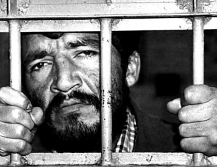 Black and white photo of a man behind prison bars symbolizing the monster who strangled over 100 young girls now free. Black and white photo of a man behind prison bars symbolizing the monster who strangled over 100 young girls now free.