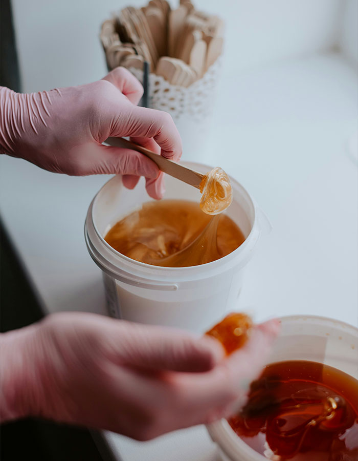 Aesthetician wearing pink gloves handling golden wax during beauty treatment in a clean, bright workspace. Aesthetician wearing pink gloves handling golden wax during beauty treatment in a clean, bright workspace.