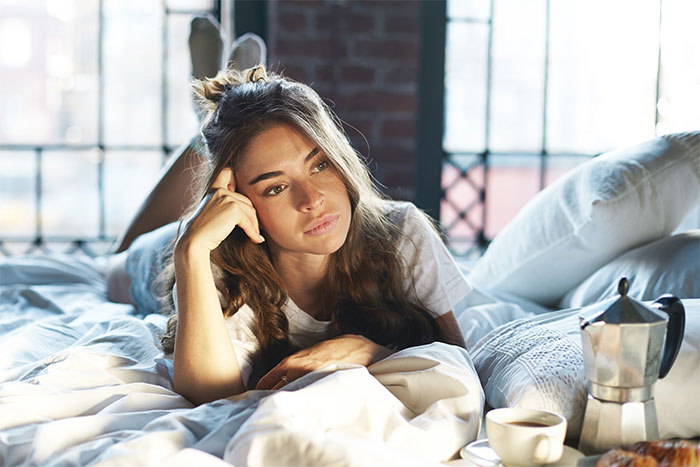 Young woman lying on bed looking thoughtful with coffee and teapot nearby in a cozy bedroom setting. Young woman lying on bed looking thoughtful with coffee and teapot nearby in a cozy bedroom setting.