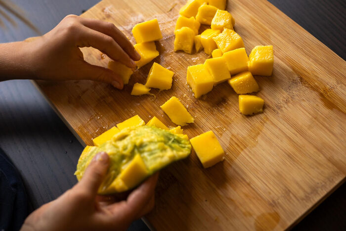 Hands cutting and separating mango pieces on a wooden cutting board showing life hacks that reveal extra work.