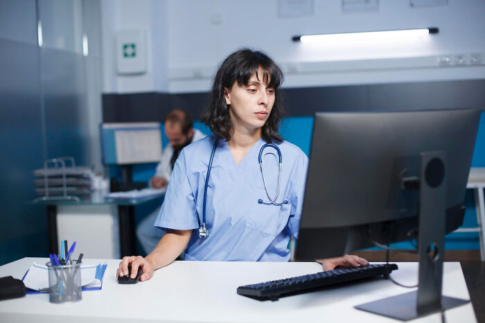 Female nurse working late on computer in hospital office, conveying scary ghost stories hospital work atmosphere.