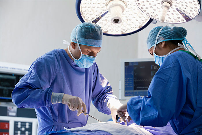 Two surgeons in an operating room performing urgent surgery related to a man with a 4-lb face tumor. Two surgeons in an operating room performing urgent surgery related to a man with a 4-lb face tumor.