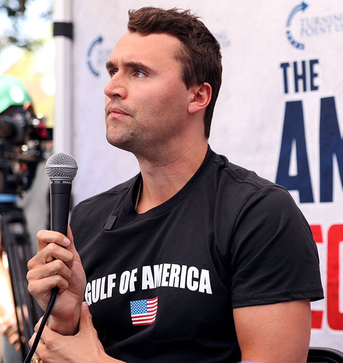 Man holding microphone wearing black Gulf of America shirt discussing Charlie Kirk life homework assignment controversy Man holding microphone wearing black Gulf of America shirt discussing Charlie Kirk life homework assignment controversy