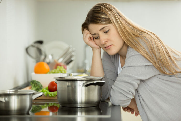 Young woman looking distressed in kitchen, highlighting unfair relationships influenced by gender roles and expectations