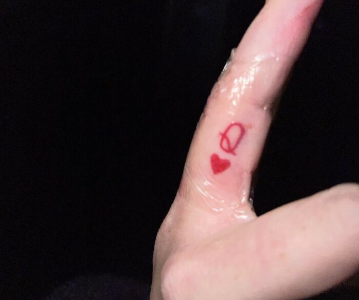 Small red tattoo of a heart and an unclear symbol on a finger, showing a unique example from tattoo artists drawing the line.