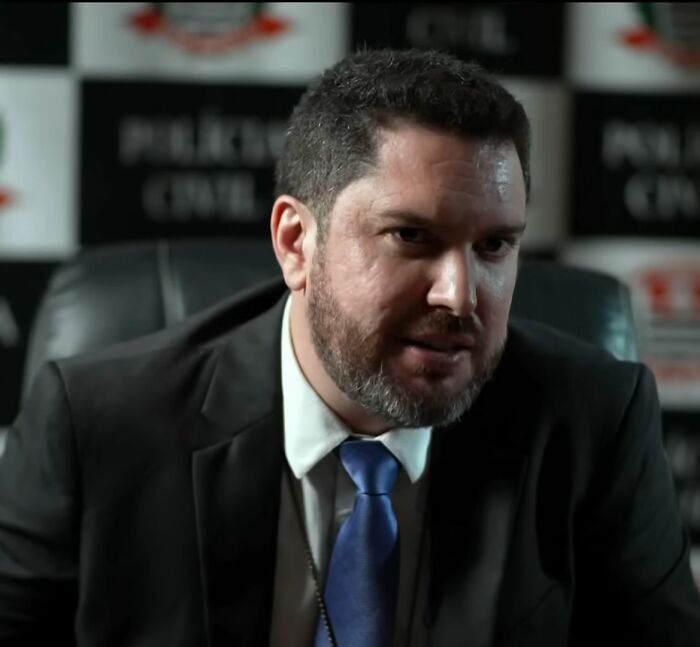 Man in a suit and blue tie giving a chilling confession about an angel-faced serial criminal in a dimly lit office setting. Man in a suit and blue tie giving a chilling confession about an angel-faced serial criminal in a dimly lit office setting.