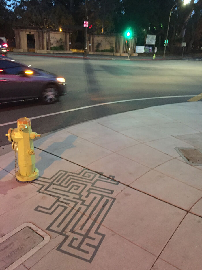 Yellow fire hydrant casting a clever shadow art installation on sidewalk in an urban street setting at night.
