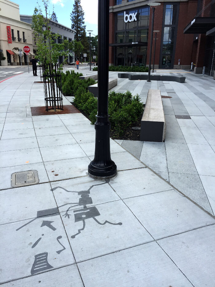 Streetlamp with clever shadow art installation on sidewalk creating a playful figure coming alive from shadows.