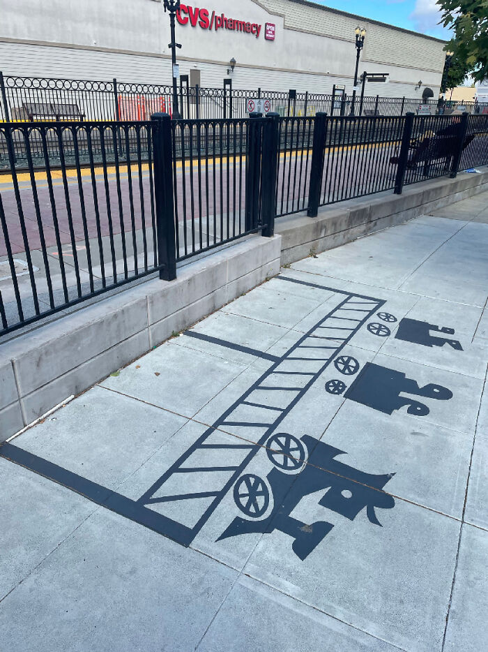 Sidewalk painted shadow art installation of a vintage train with a ladder, wheels, and silhouetted figures on a city street.