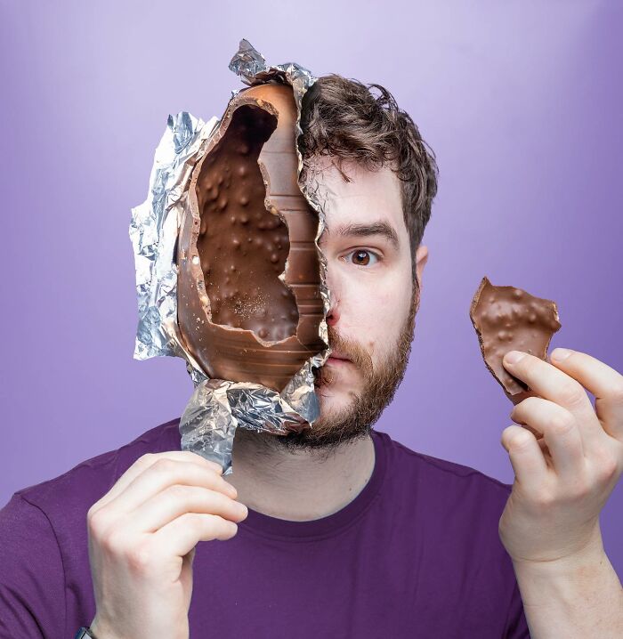 Man holding a logic-challenging photo manipulation of half his face made of chocolate in foil against a purple background
