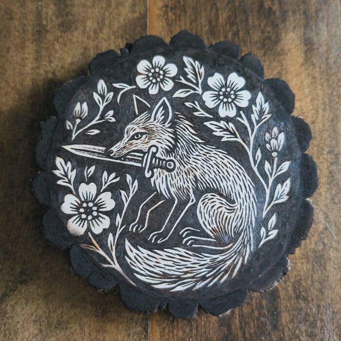Wood-burned artwork by Canadian artist Kat Slota featuring a detailed fox holding a sword surrounded by floral designs.
