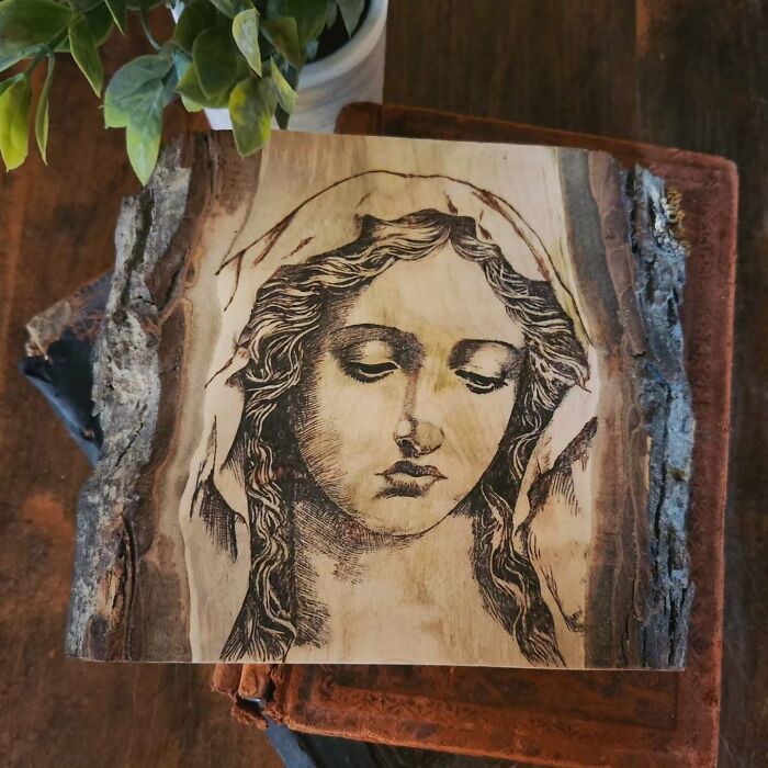 Wood-burned artwork of a woman's face on a natural bark wood slice by Canadian artist Kat Slota using fire.