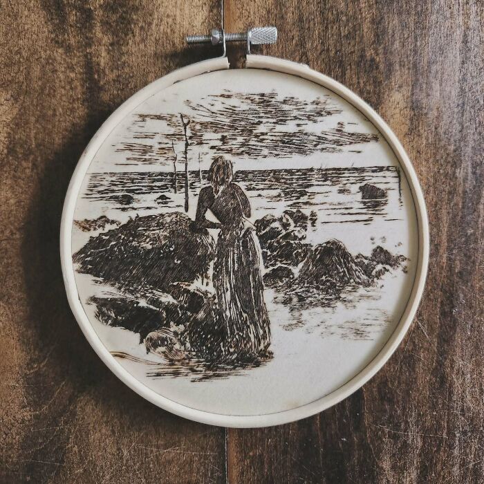 Wood-burned artwork by Canadian artist Kat Slota depicting a woman standing near rocks by the sea using fire.