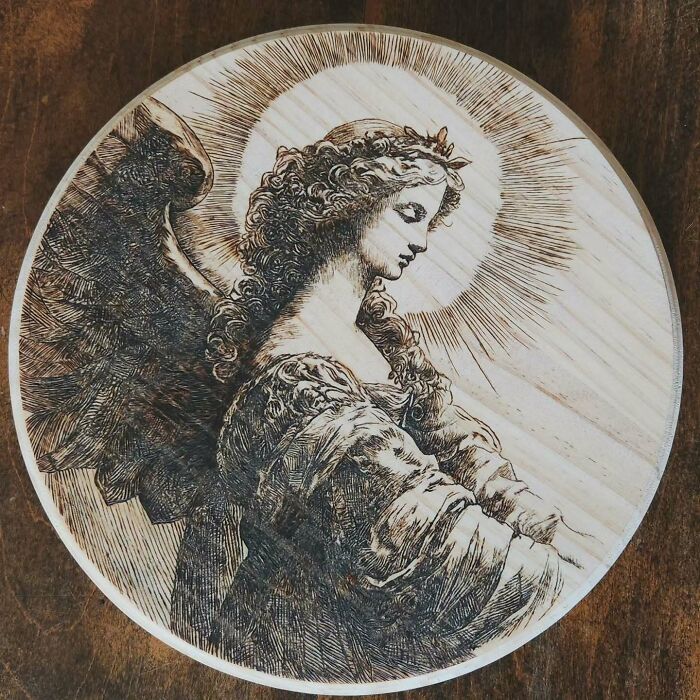 Wood-burned artwork of an angel with a halo, created using fire by Canadian artist Kat Slota on a round wooden panel.