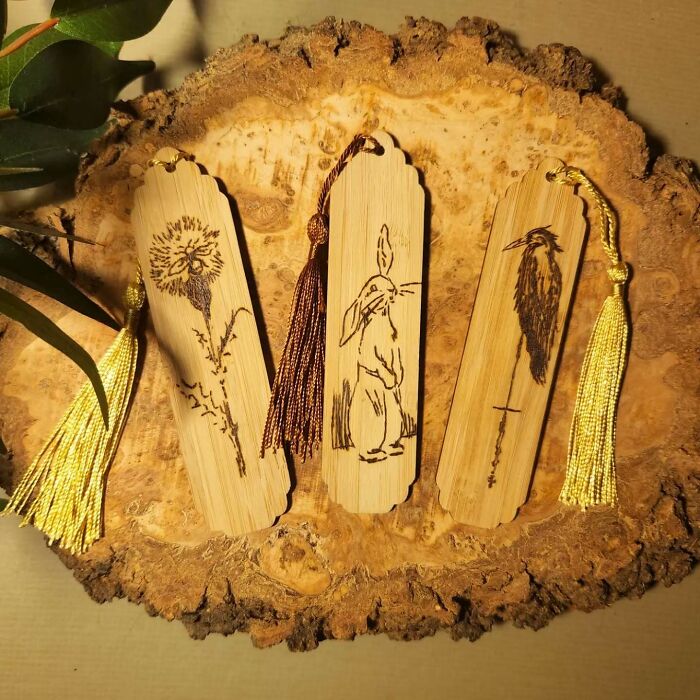 Three wood-burned bookmarks featuring a flower, rabbit, and bird, showcasing Canadian artist Kat Slota’s fire art technique.