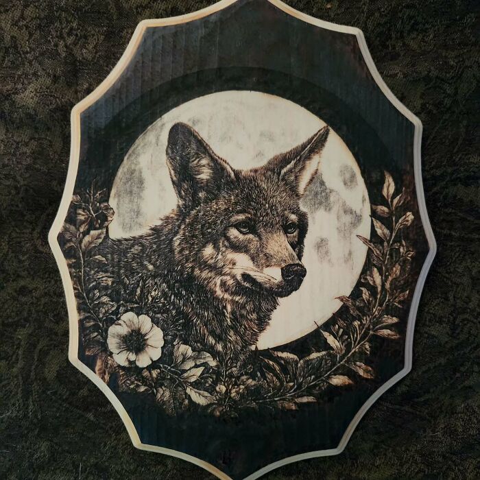 Wood-burned artwork of a wolf framed by flowers and leaves, created by Canadian artist Kat Slota using fire.