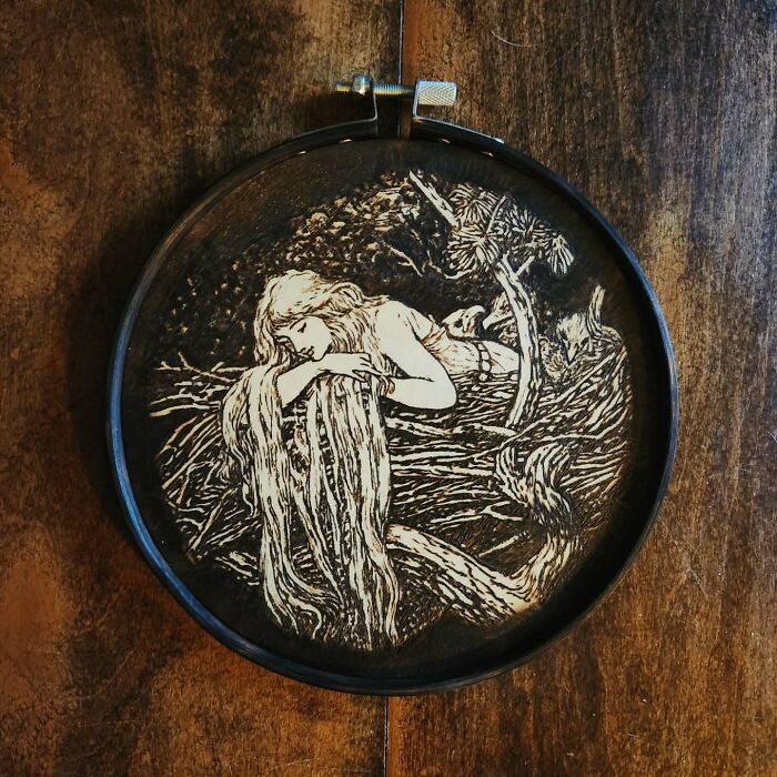 Wood-burned artwork by Canadian artist Kat Slota depicting a woman resting with flowing hair on a textured wooden surface.