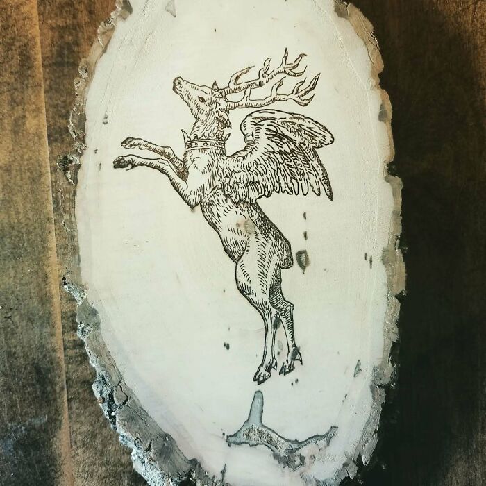 Wood-burned artwork of a winged stag on a natural wood slice by Canadian artist Kat Slota using fire techniques.