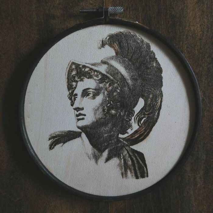 Wood-burned artwork of a classical figure with a feathered helmet created by Canadian artist Kat Slota using fire.