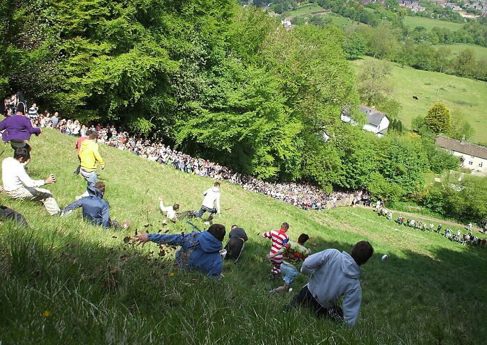 Participants racing down a steep hill during a dangerous and unsafe traditional historical sport event with large crowds watching.