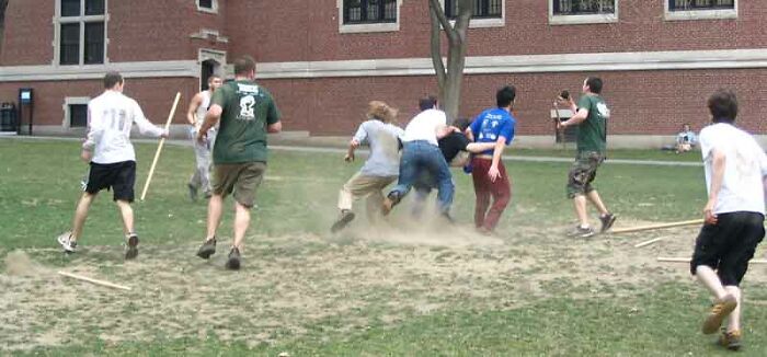 Group of young men running and colliding on dusty grass field playing a dangerous and unsafe historical sport.