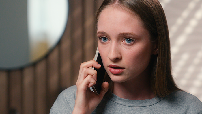 Young woman with serious expression on phone call, depicting sister revealed dead brother lie theme in a home setting.