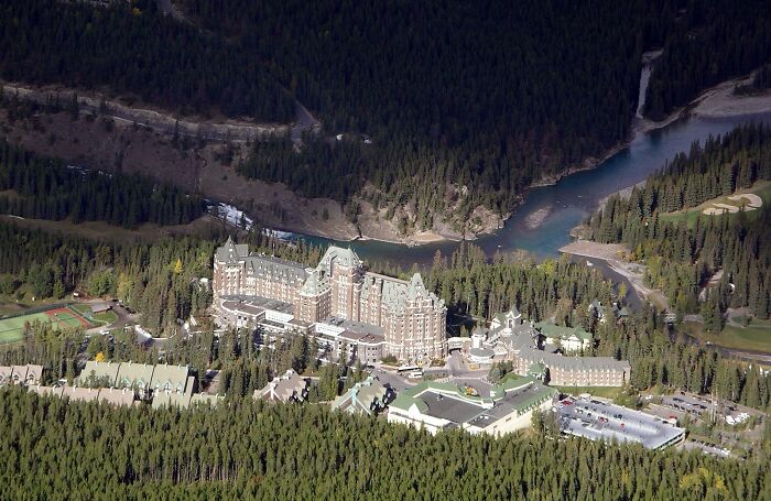 Aerial view of a large historic castle surrounded by dense forest and a winding river, a spooky destination for Halloween.