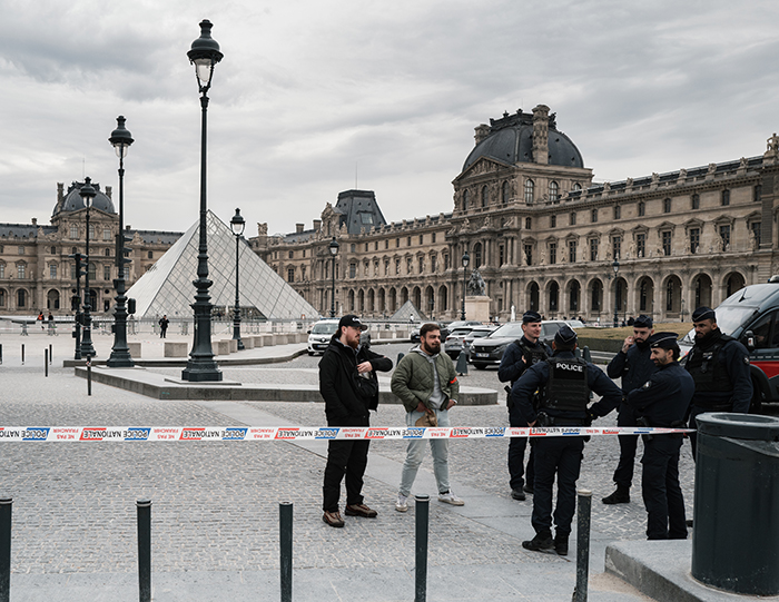 Police officers and bystanders gathered near the Louvre, discussing security after notorious jewel thief alerts on smuggling trick. Police officers and bystanders gathered near the Louvre, discussing security after notorious jewel thief alerts on smuggling trick.