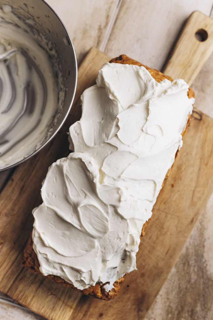 Butternut squash autumn cake on wooden board being frosted with creamy cinnamon-spiced icing in a metal bowl nearby Butternut squash autumn cake on wooden board being frosted with creamy cinnamon-spiced icing in a metal bowl nearby