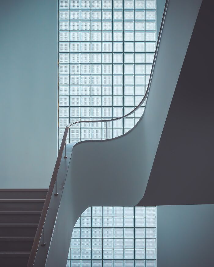 Minimalist architectural design by Olle L featuring a sleek staircase and large glass block window with natural light.