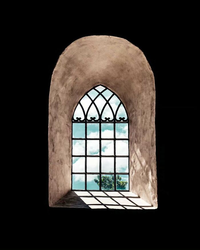 Arched minimalist architectural window with decorative grid casting shadows inside a simple textured wall.