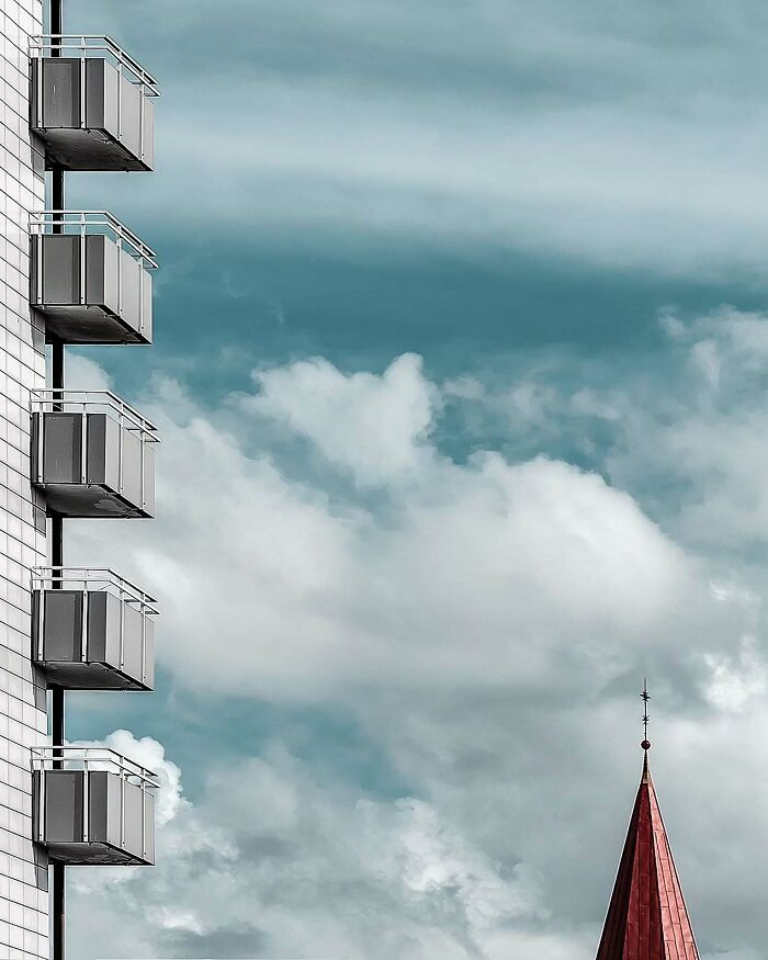 Minimalist architectural vision shown in a modern building with clean lines and balconies against a cloudy sky.