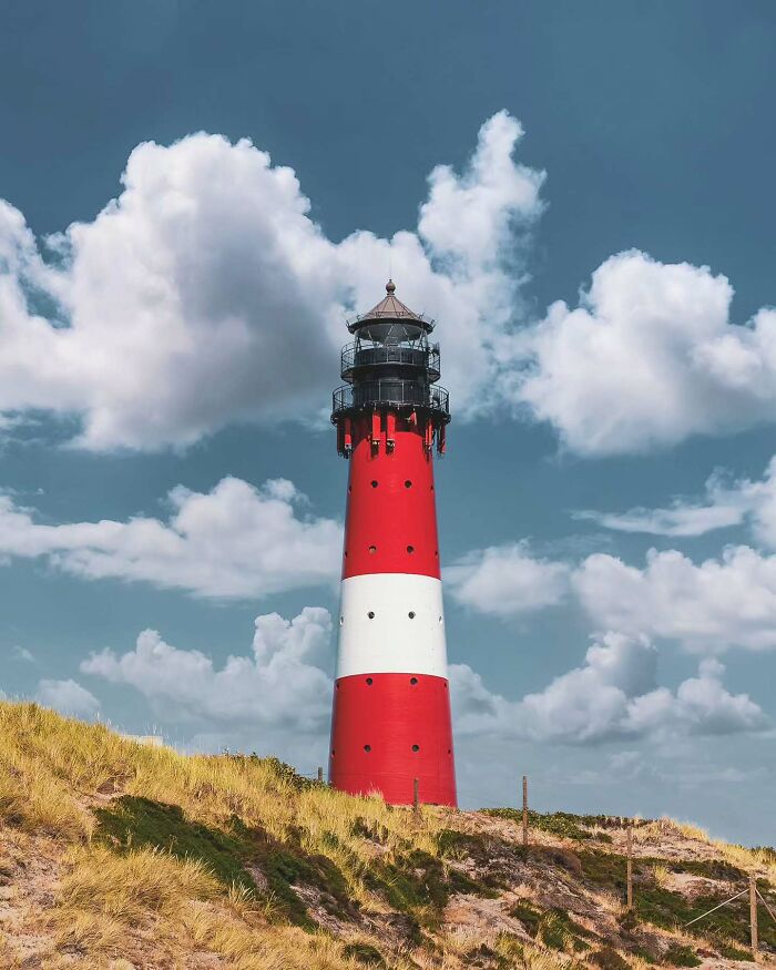 Red and white lighthouse standing tall on grassy dunes under a blue sky, showcasing minimalist architectural vision.