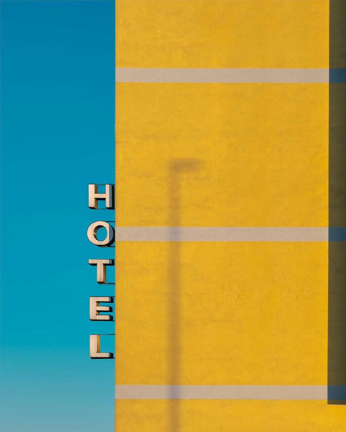 Minimalist architectural vision shown in a yellow building facade with hotel signage against a clear blue sky.