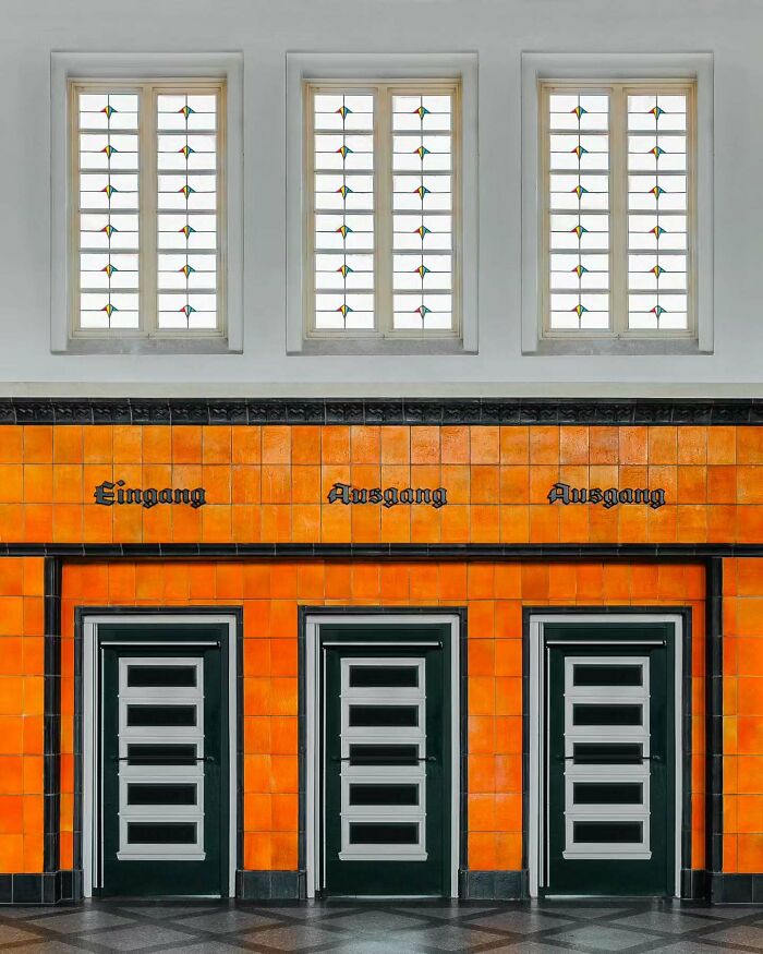 Three minimalist doors with orange tiled walls and white framed windows showcasing minimalist architectural design.