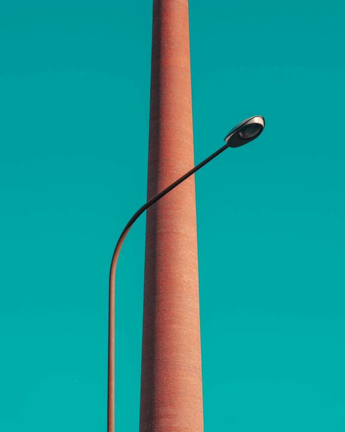 Minimalist architectural vision shown in a tall brick column with a curved street lamp against a clear blue sky.