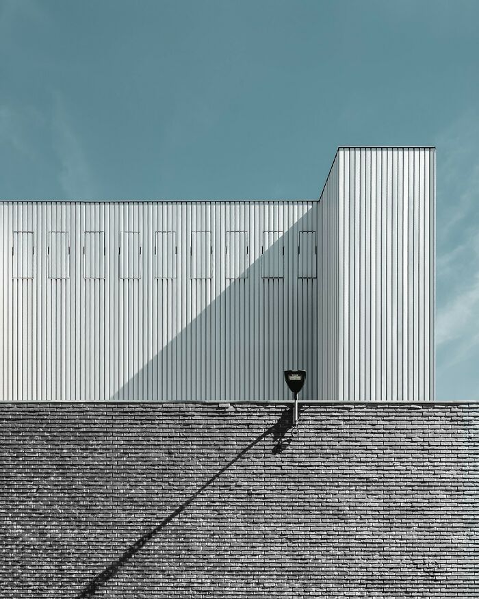 Minimalist architectural design by Olle L featuring clean lines, geometric shapes, and contrasting textures under a clear blue sky.
