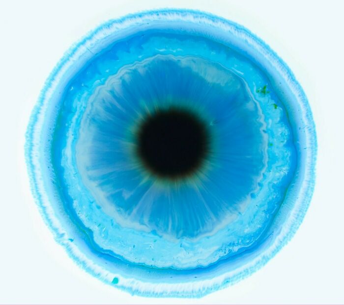 Close-up image of blue ink in water forming a hypnotic pattern resembling a human eye iris and pupil.