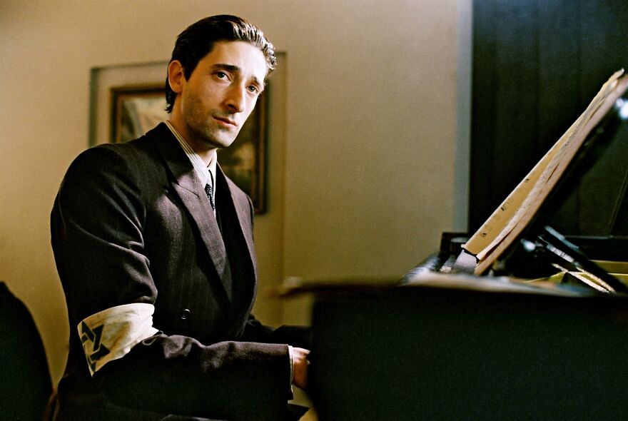 Actor in a period costume playing piano in a movie based on true stories that feel impossible to believe.