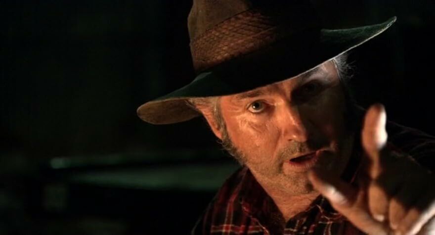A man in a dark hat and plaid shirt pointing forward in a dramatic scene from movies based on true stories.