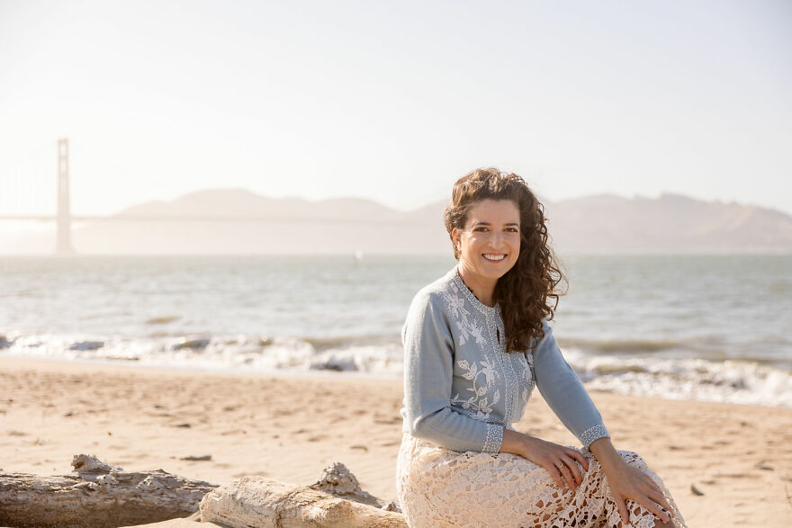 Woman sitting on beach smiling with ocean and distant bridge, representing billboard campaign to find love responses. Woman sitting on beach smiling with ocean and distant bridge, representing billboard campaign to find love responses.