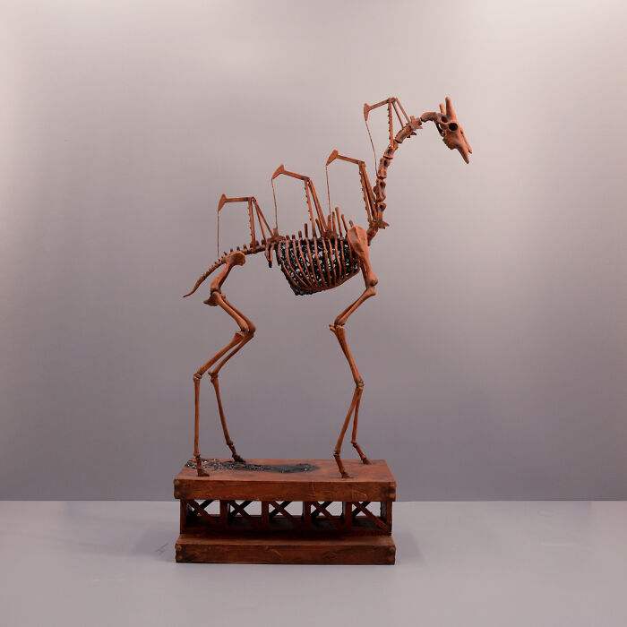 Haunting porcelain sculpture resembling a mythical creature’s skeletal relic on a wooden base in a minimalist setting