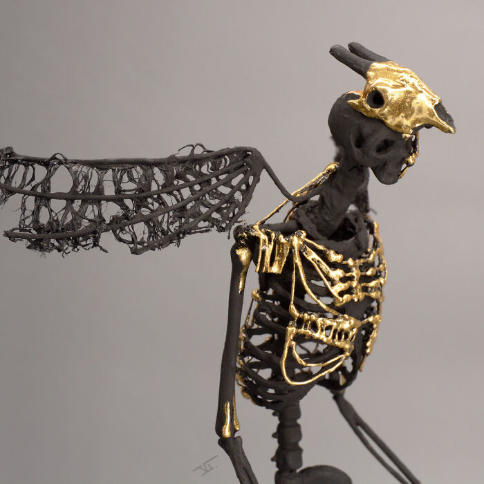 Haunting porcelain sculpture of a skeletal mythical creature with gold accents and delicate lace-like wings on a neutral background.