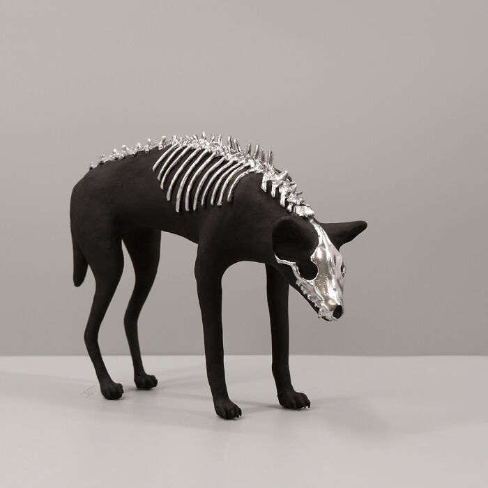 Black porcelain sculpture of a dog with silver skeletal details, evoking haunting relics of forgotten myths.
