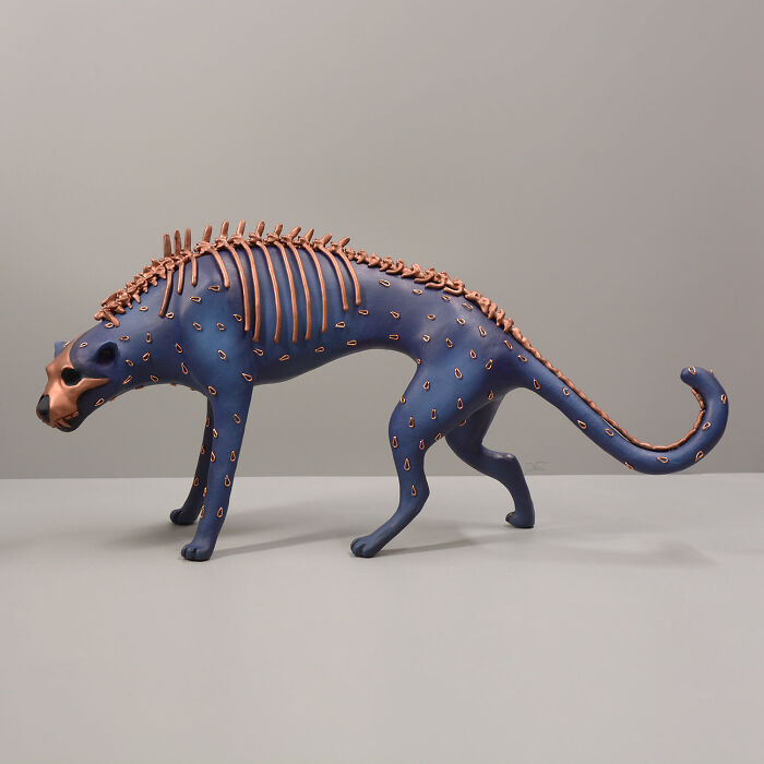 Haunting porcelain sculpture of a mythical animal with copper-colored bones and blue spotted body on a neutral background.