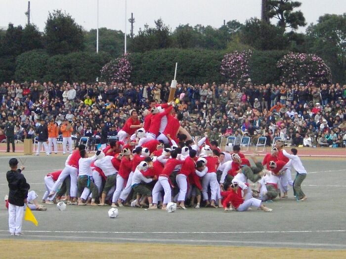 A group of people in red and white uniforms engaged in a chaotic, dangerous historical sports event outdoors.